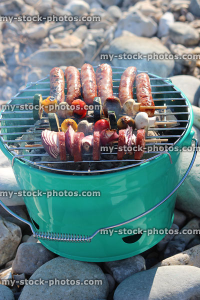 Stock image of green metal barbecue cooking sausages on beach, smoking hot coals