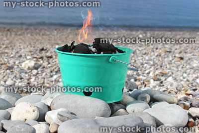 Stock image of charcoal barbecue flames in painted bucket on beach