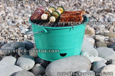 Stock image of charcoal barbecue on beach, sausages, vegetable kebabs, mushrooms