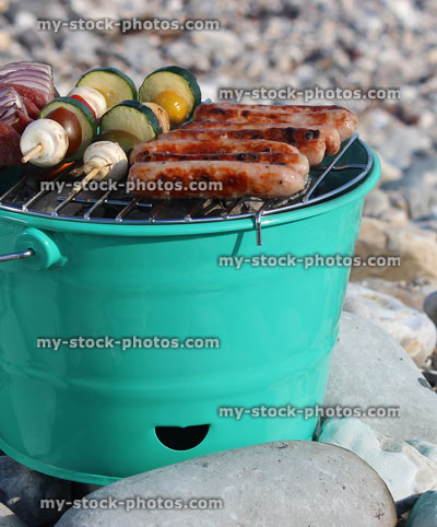 Stock image of bucket barbecue with sausages, vegetable kebabs, on pebbles