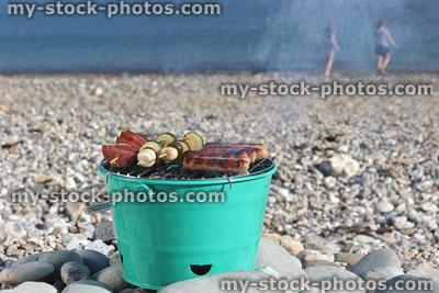 Stock image of smoky beach barbecue bucket cooking sausages, children playing