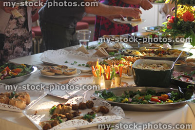 Stock image of people serving themselves, buffet table of party food