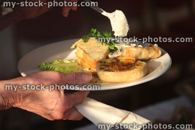 Stock image of buffet, person piling plate with party food, sandwich, mini quiche