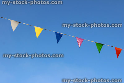 Stock image of row of rainbow coloured bunting flags on rope, against blue sky