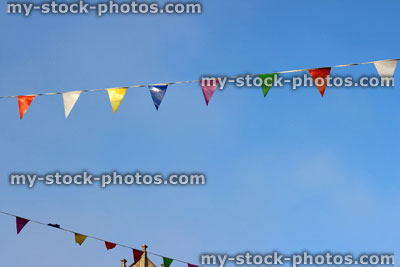 Stock image of row of rainbow coloured bunting flags on rope, against blue sky
