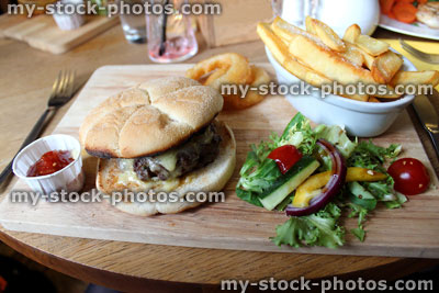 Stock image of gourmet cheeseburger, chunky chips, onion rings and salad