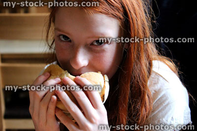Stock image of young girl eating a cheese burger / beef burger in bap