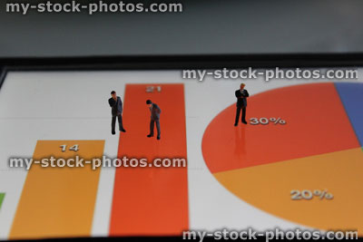 Stock image of mini businessmen looking at colourful graphs on tablet computer screen