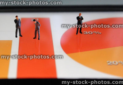 Stock image of mini businessmen looking at colourful graphs on tablet computer screen