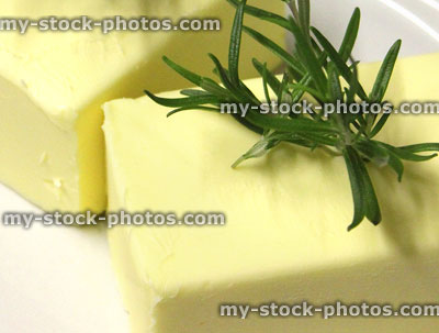 Stock image of blocks of fresh butter, sprigs of rosemary herb
