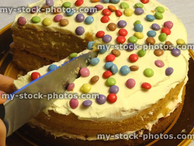Stock image of cutting / slicing homemade sponge cake, decorated with icing, chocolate sweets, cake slice