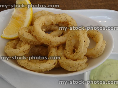 Stock image of crispy deep fried calamari rings with lemon wedge, mayonnaise
