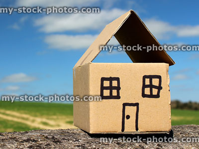 Stock image of small brown cardboard house / homemade dollshouse, field / sky background