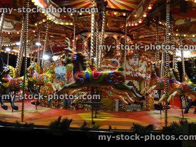Stock image of moving carousel roundabout with painted horses at night
