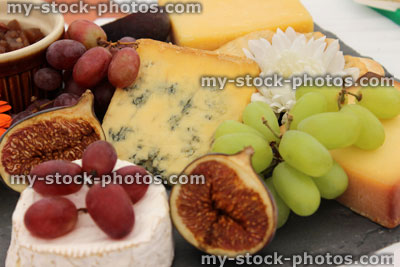 Stock image of slate cheese board, Stilton, Cheddar cheese, grapes, figs, crackers, flowers