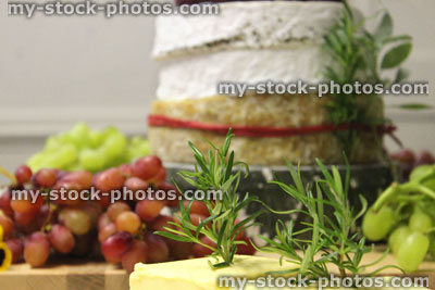 Stock image of stack of cheeses / cheese cake, wooden board, seedless grapes, butter