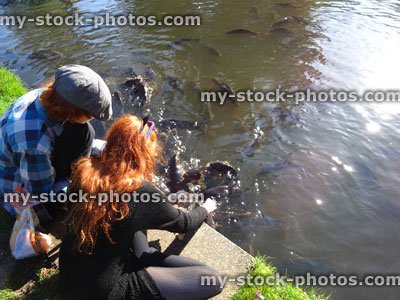 Stock image of children feeding koi and common carp / splashing in lake