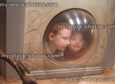 Stock image of young children looking through porthole window at zoo