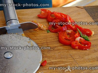 Stock image of sliced red chilies on breadboard with pizza wheel