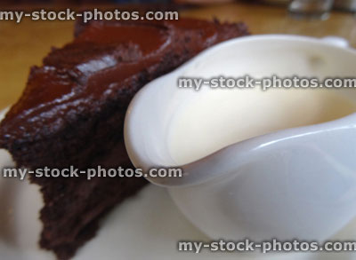 Stock image of homemade chocolate fudge cake slice, jug of cream, ganache butter icing