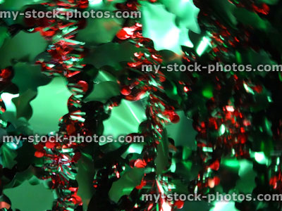 Stock image of defocussed coloured tinsel Christmas decorations, green holly leaves, red berries garland