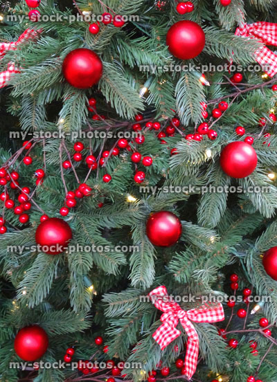 Stock image of artificial Christmas tree, red decorations, garlands, baubles, tinsel, berries, ribbons, bows, fairy lights