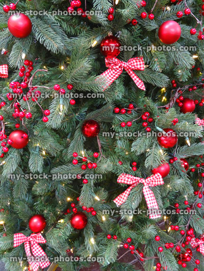 Stock image of artificial Christmas tree, red decorations, garlands, baubles, tinsel, berries, ribbons, bows, fairy lights