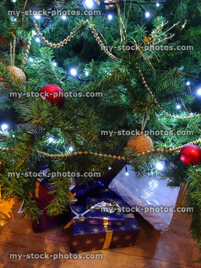 Stock image of artificial Christmas tree, red / gold decorations, baubles, chains, wrapped presents / gifts