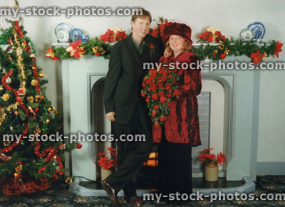 Stock image of Christmas wedding, husband and wife (crushed red velvet jacket), fireplace, Christmas tree decorations