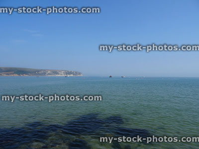 Stock image of seaside coastline with clear blue shallow water, distant cliffs