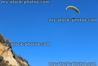 Stock image of paraglider in blue sky flying over sandy cliffs