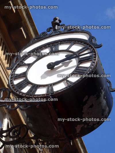 Stock image of outdoor metal clock outside shop with Roman numerals