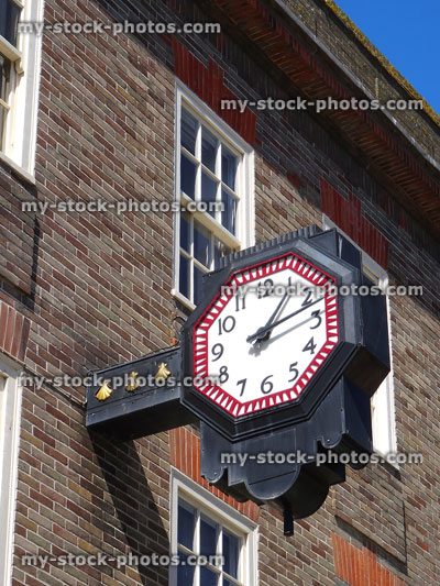 Stock image of numbered wall clock hanging above shop-front, town centre