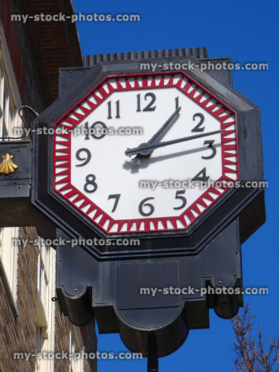 Stock image of octagonal metal clock hanging above shop, against sky