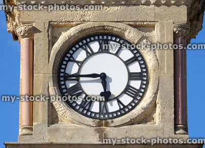 Stock image of stone clock tower with white clockface, Roman numerals