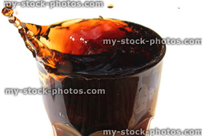 Stock image of ice being dropped into fizzy cola glass, splash