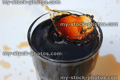 Stock image of ice being dropped into fizzy cola glass, splash