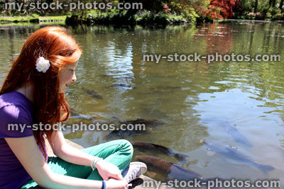 Stock image of girl sat next to lake, with koi carp swimming by