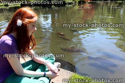 Stock image of girl sat next to lake, with koi carp swimming by