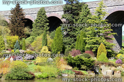 Stock image of rock garden with conifers next to pond water 