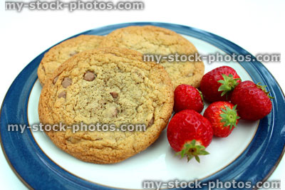Stock image of large homemade chocolate chip cookies, served with strawberries