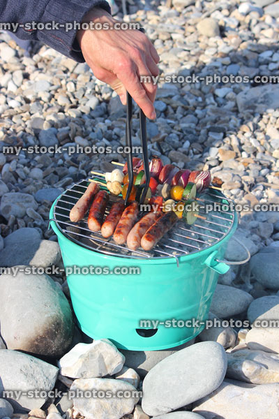 Stock image of bucket barbecue on beach, sausages being turned using tongs
