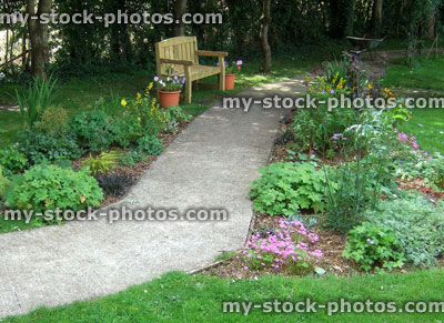 Stock image of shady, woodland style country garden, concrete pathway through flowerbed