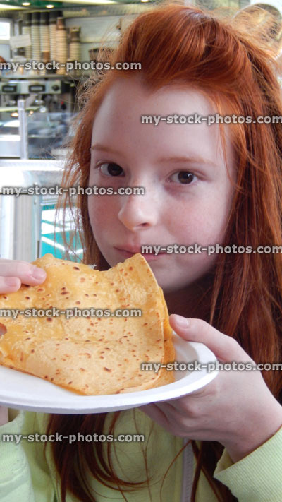 Stock image of girl eating fresh crepe at cafe / fastfood takeaway kiosk