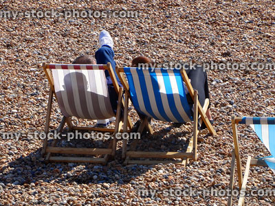 Stock image of couple sitting in striped deckchairs on pebble beach