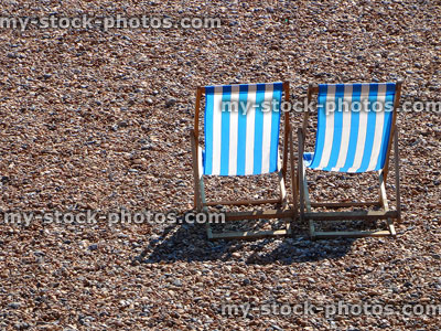 Stock image of two blue / white striped seaside deckchairs on pebble-beach