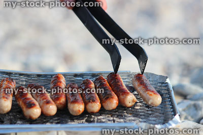 Stock image of chipolata sausages being turned on disposable foil barbecue