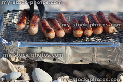Stock image of sausages burning turned with tongs, disposable lumpwood barbecue