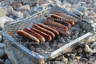 Stock image of smoking beach barbecue cooking sausages, disposable bbq charcoal