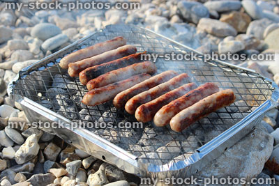 Stock image of disposable charcoal barbecue cooking sausages at beach picnic